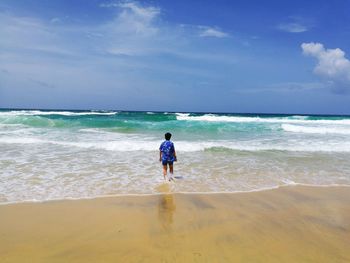 Rear view of man standing on beach against sky