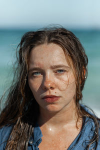 Female in wet shirt and with wet hair standing looking at camera on beach near sea while enjoying summer day