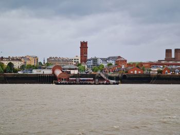 Buildings by river against sky in city