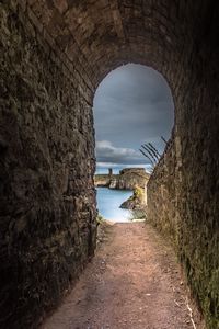 Footpath amidst sea seen through tunnel