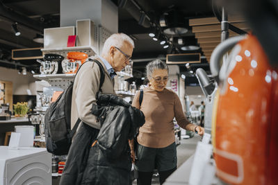 Elderly couple examining appliances while shopping in modern electronics store