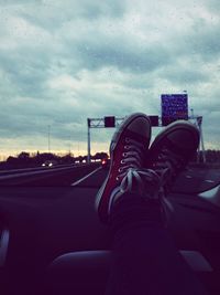 Low section of person on dashboard in car against cloudy sky