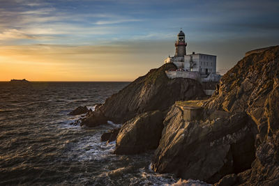 Lighthouse by sea against sky during sunset