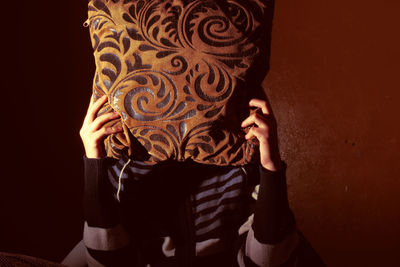 Woman covering face with cushion against wall