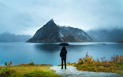 Rear view of woman holding umbrella standing against lake