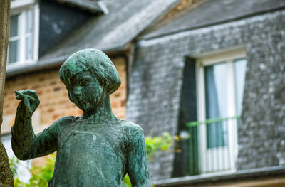 Statue of a girl writing, with defocused background of typical house of the french brittany