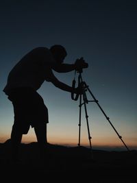 Silhouette of photographer photographing on landscape during sunset
