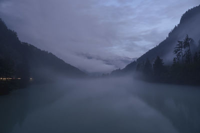 Scenic view of misty river and mountains against sky in fading daylight 