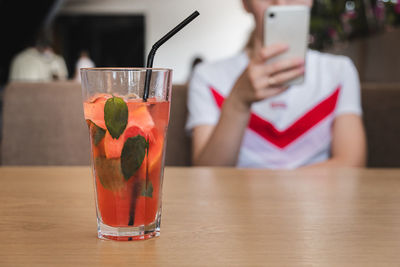 Close-up of person holding drink with laptop on table