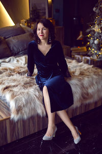 Woman in blue long dress sitting on bed at christmas