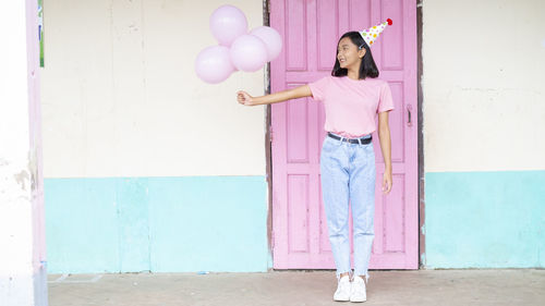 Full length of woman with pink balloon standing against wall