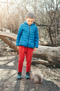 Cute caucasian boy feeding grey squirrel in park.  kid giving food nuts to wild animal in forest