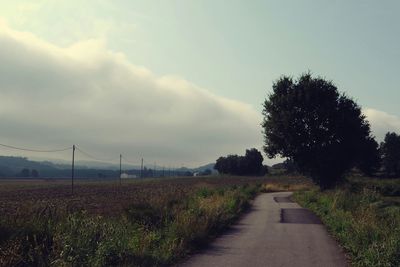 Road passing through field against cloudy sky