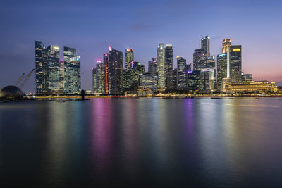 Illuminated modern buildings in city against sky at night