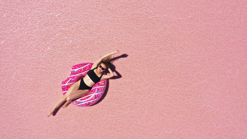 Aerial view of beautiful woman lying in a bikini on inflatable mattress on pink salt lake. 