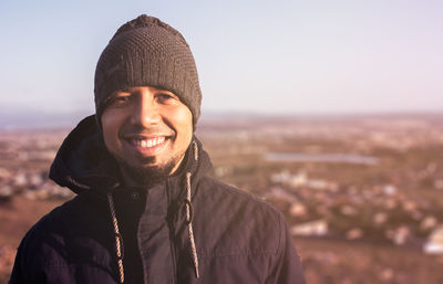 Portrait of smiling young man wearing knit hat against sky