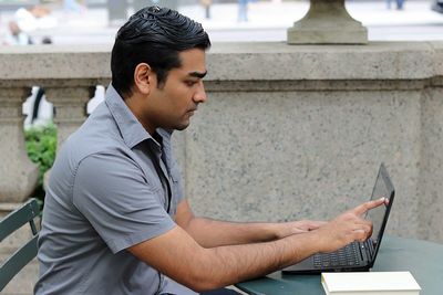 Side view of young man using laptop at sidewalk cafe