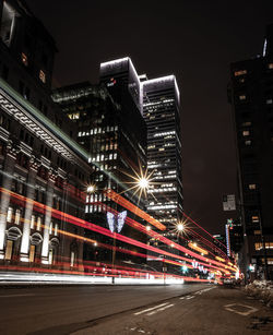 Illuminated city street and buildings against sky at night