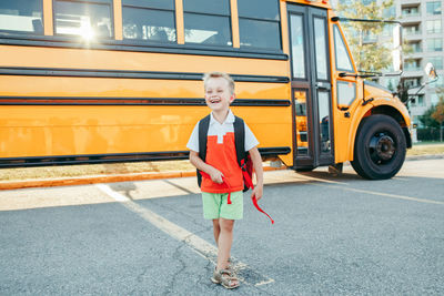 Cheerful boy walking against school bus
