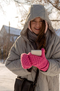 Woman with freckles in winter clothes with mittens outdoors uses her smartphone and smiles