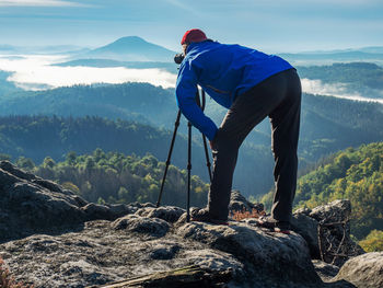 Bent photographer framing scene in viewfinder. man is using camera on tripod for taking pictures