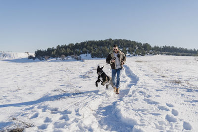 Playful man with dog running in snow on sunny day