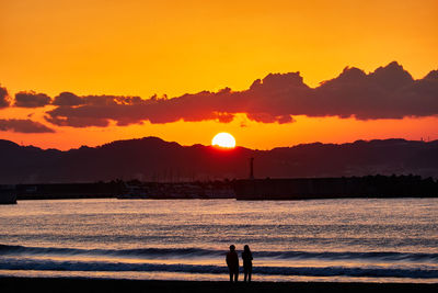 Silhouette people on beach against sky during sunrise