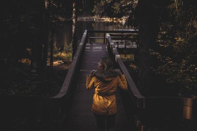 Rear view of woman standing on footbridge by trees