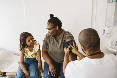 Mother talking with daughter while male doctor measuring blood pressure