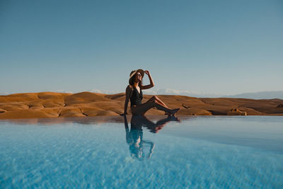 Full length of woman sitting by water against sky