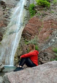 Woman sitting on rock looking at waterfall