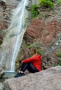 Man sitting on rock looking at waterfall