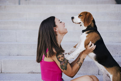 Side view of happy woman playing with dog while sitting on steps