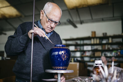 Senior man decorating ceramic vase in his spare time