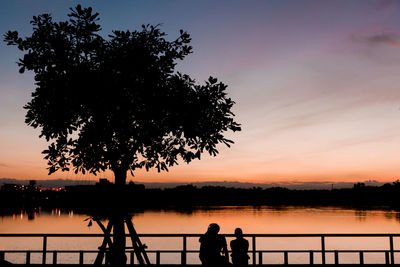 Silhouette people standing by lake against sky during sunset