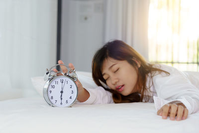 Woman holding alarm clock while sleeping on bed at home