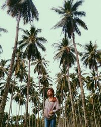 Portrait of young woman standing on palm tree against clear sky