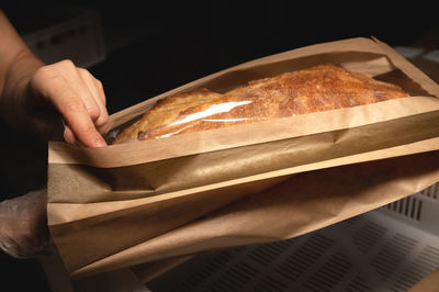 Women's caring hands pack fresh artisan bread in a paper bag with a transparent insert
