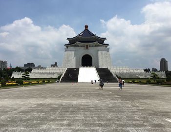 People in front of historical building against cloudy sky