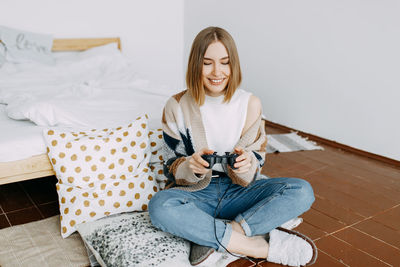A girl in casual clothes plays on a video console sitting on the floor in the bedroom at home