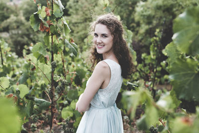 Beautiful smiling curly hair brunette in a light blue simple dress in a vineyard