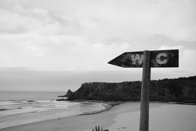 Signboard at beach against sky