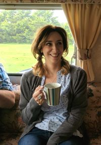 Happy mid adult woman having drink while sitting at home