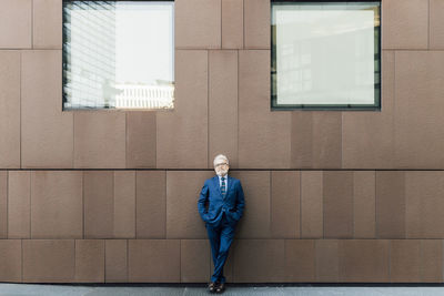 Senior businessman standing with hands in pockets outside building exterior