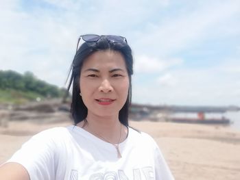 Portrait of smiling young woman on beach against sky