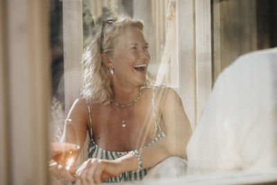 Happy woman looking away during dinner party seen through cafe window