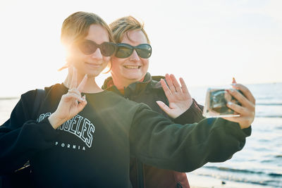 Women making gesture and waving during video call on smartphone during trip on summer vacation