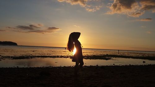 Silhouette of woman standing on beach at sunset