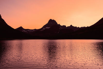 Scenic view of lake by silhouette mountains against sky during sunset