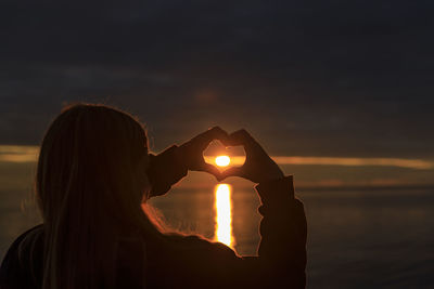 Silhouette woman holding sun by sea against sky during sunset